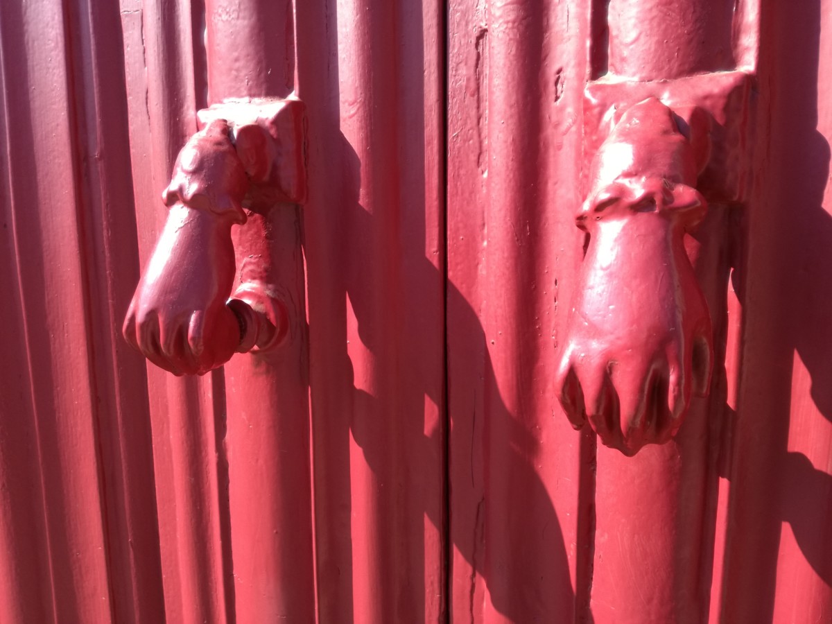 Een roze deur met twee handjes in dezelfde kleur die wel op kinderknuistjes lijken.