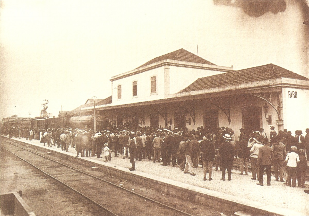 Zwart-witfoto van het treinstation van Faro. Er staan veel mensen op het perron te wachten. 