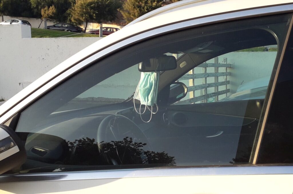 Twee maskertjes hangend aan de binnenspiegel van een geparkeerde auto. 