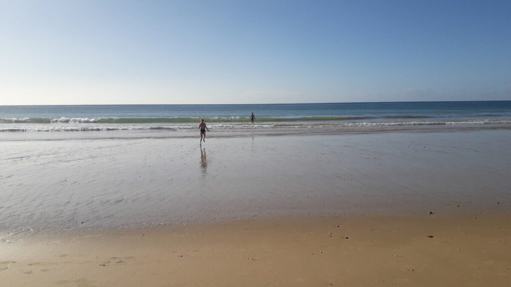 Foto van twee kinderen die op een verlaten strand in de Algarve in Portugal naar het water toe rennen.