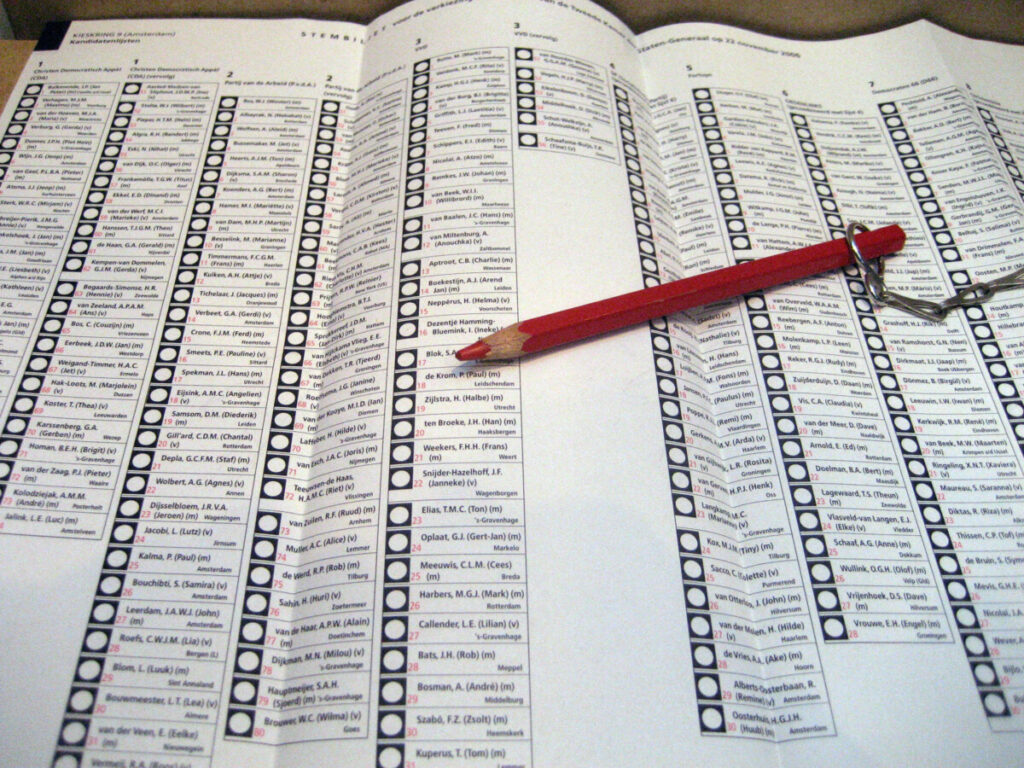 Traditioneel groot opengevouwen verkiezingsformulier met erop liggen een rood potlood.