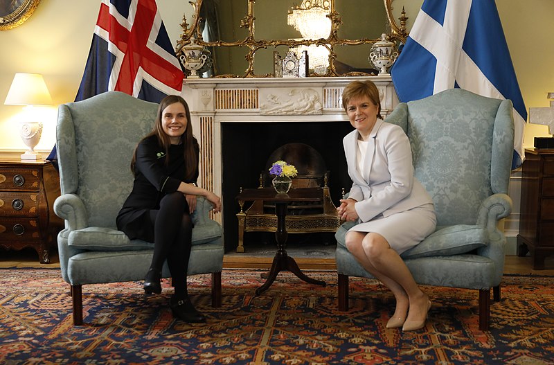 Nicola Sturgeon en Katrin Jakobsdottir gezeten voor de respectievelijke vlaggen van Schotland en IJsland. 