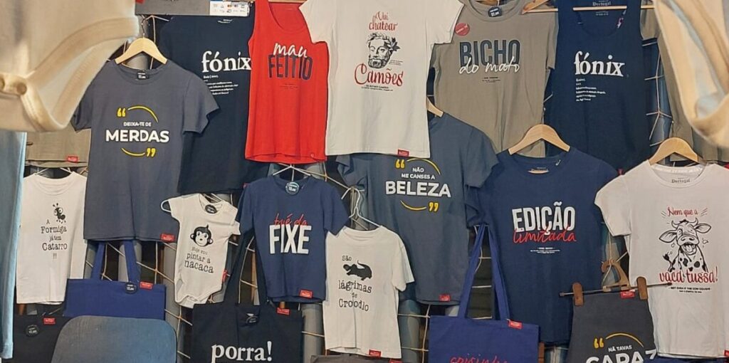 T-shirt verkoopstand met allerlei Portugese teksten waaronder mau feitio, bicho do mato, fonix, foda-se, bué da fixe, merdas, en meer