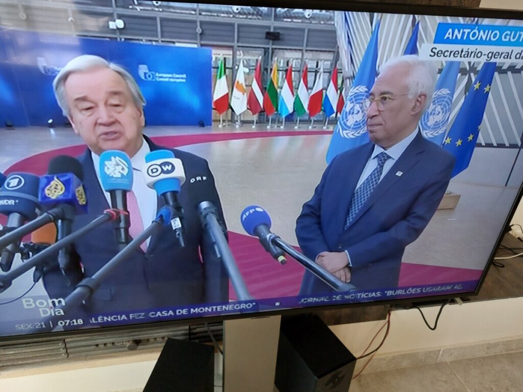 Foto van een televisiebeeld met Guterres en Costa voor een aantal vlaggen van de Verenigde Naties.