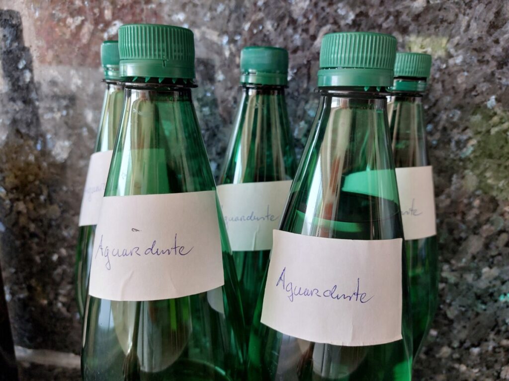 Vijf waterflessen met ieder een handgeschreven etiket 'aguardente'.