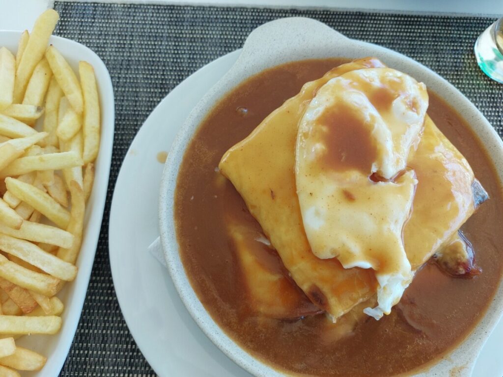 Francesinha ruim in saus met een bak friet ernaast.