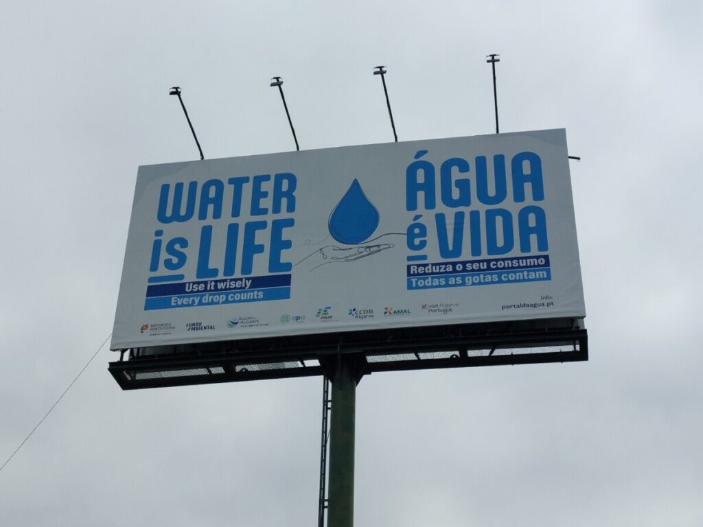 Groot bord met in twee talen (Engels en Portugees) 'Water is leven', en 'iedere druppel telt'.