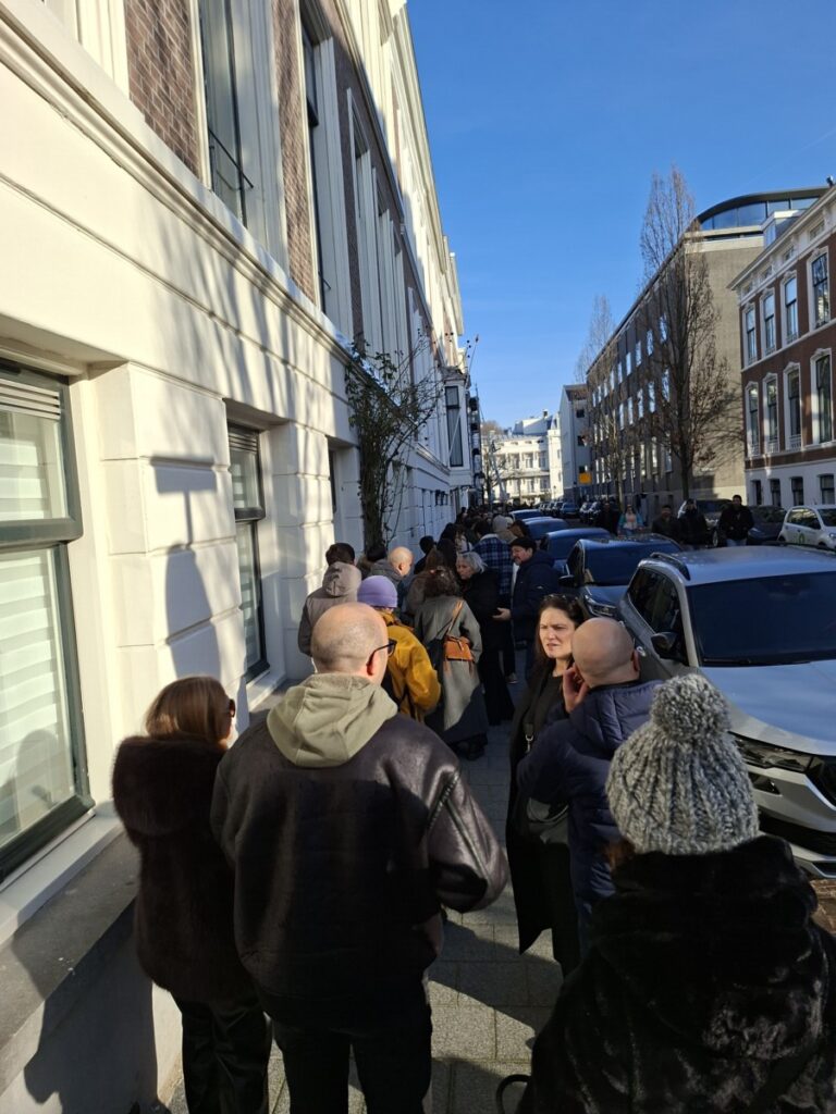 Lange rij mensen in een zonnige straat.