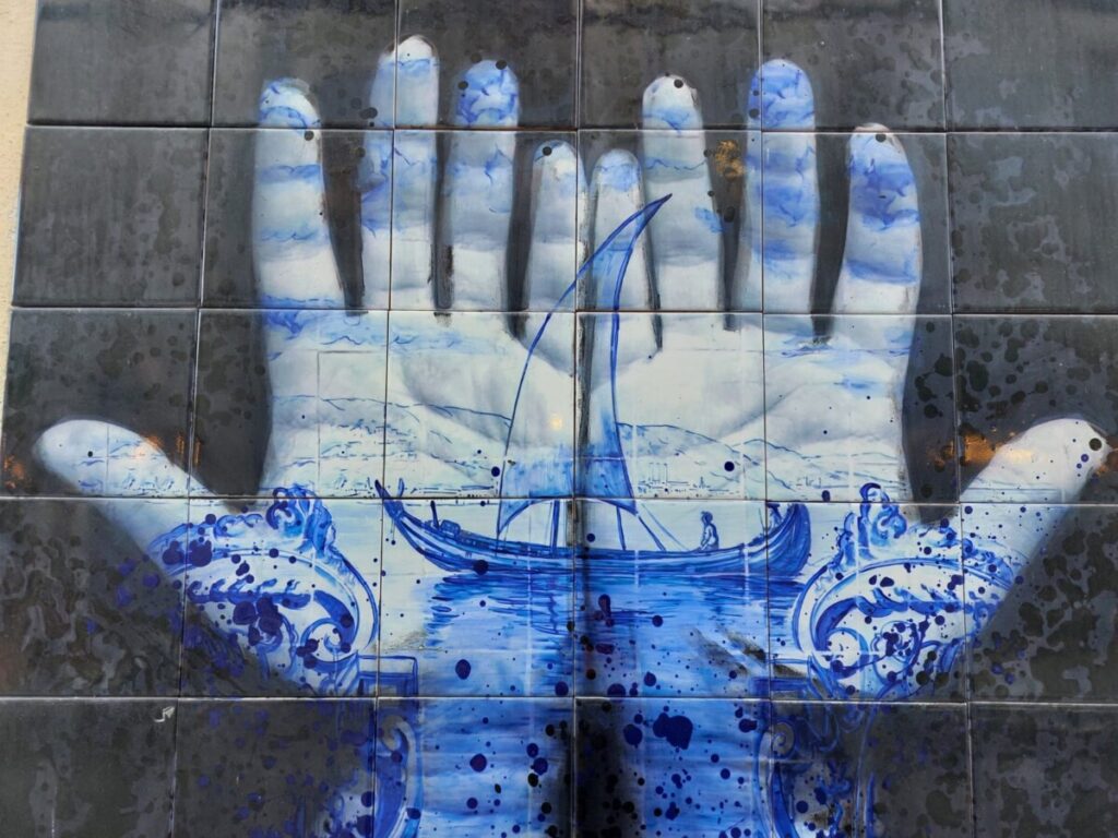 Twee  blauwe geschilderde handen met een afbeelding van een oud schip erin.