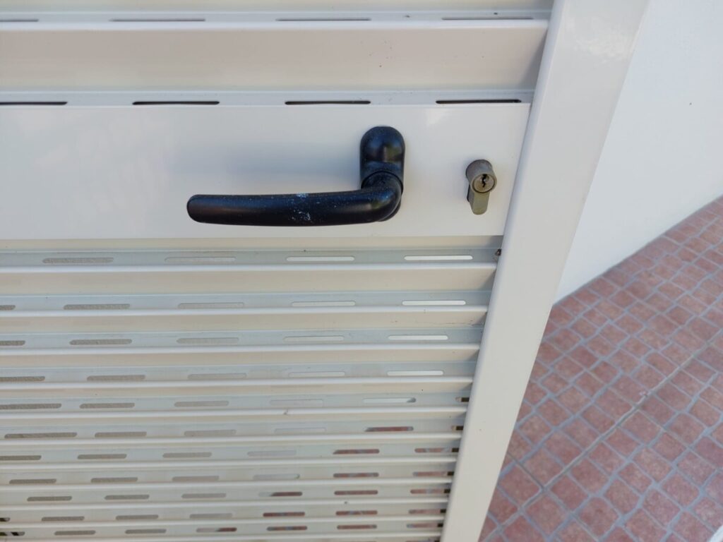 Close up van een portada met de deurklink en de sleuven aan de onderzijde waardoor lucht en licht binnen kunnen komen