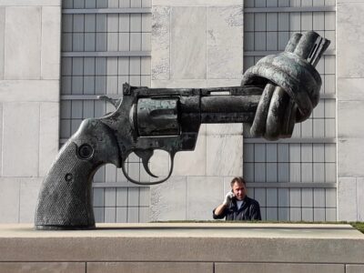 Beeldhouwwerk voor het gebouw van de VN, een revolver met een knoop in de loop. Op de achtergrond staat een man aan de telefoon te praten. Foto Cees Groenewegen
