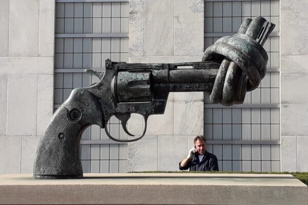 Beeldhouwwerk voor het gebouw van de VN, een revolver met een knoop in de loop. Op de achtergrond staat een man aan de telefoon te praten. Foto Cees Groenewegen
