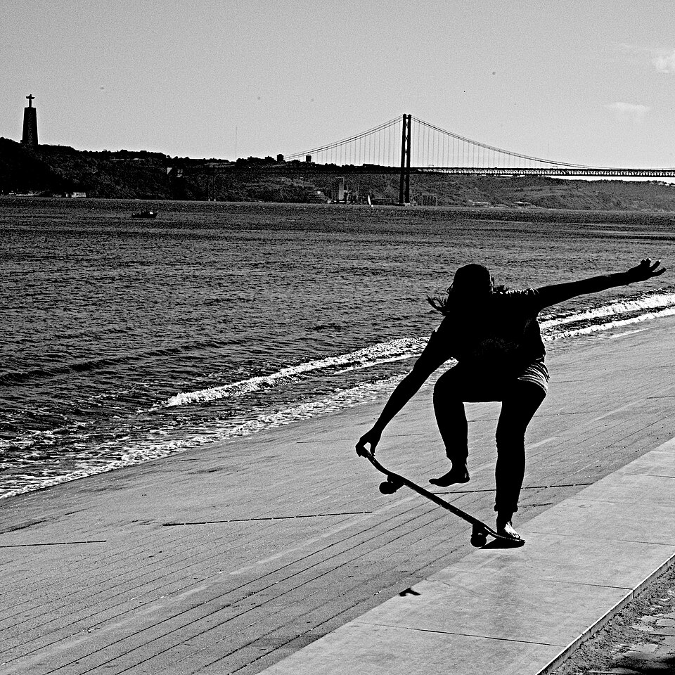 Skater met op de achtergrond de Ponte 25 de Abril en het standbeeld Cristo Rei, in Lissabon.
