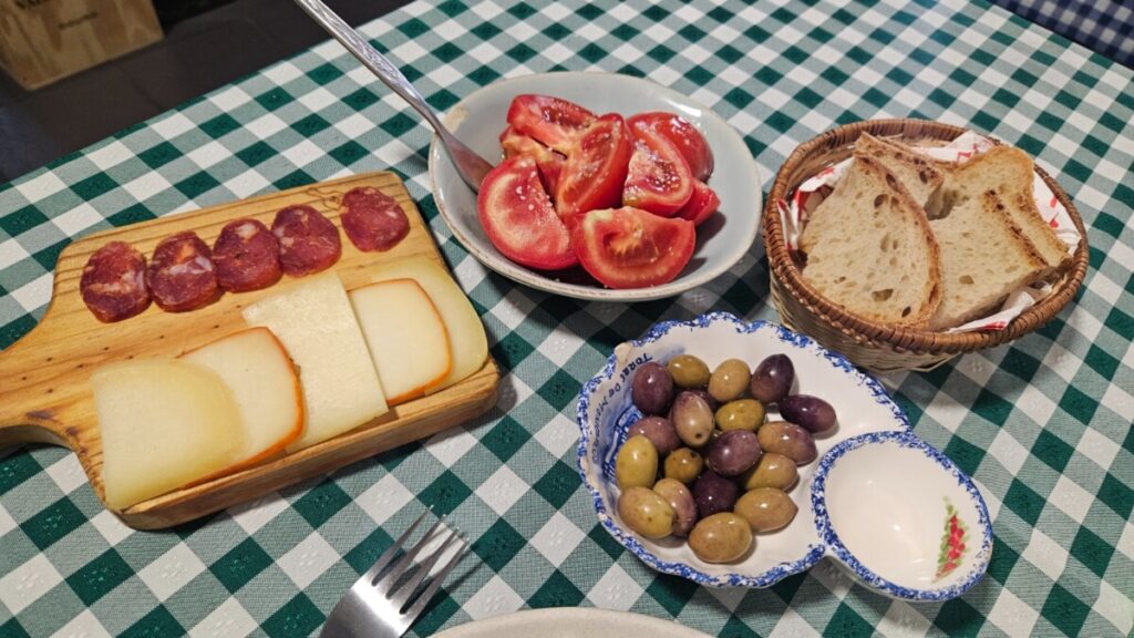Plankje met kazen en enchidos, olijven, streekbrood en gemarineerde tomaat.