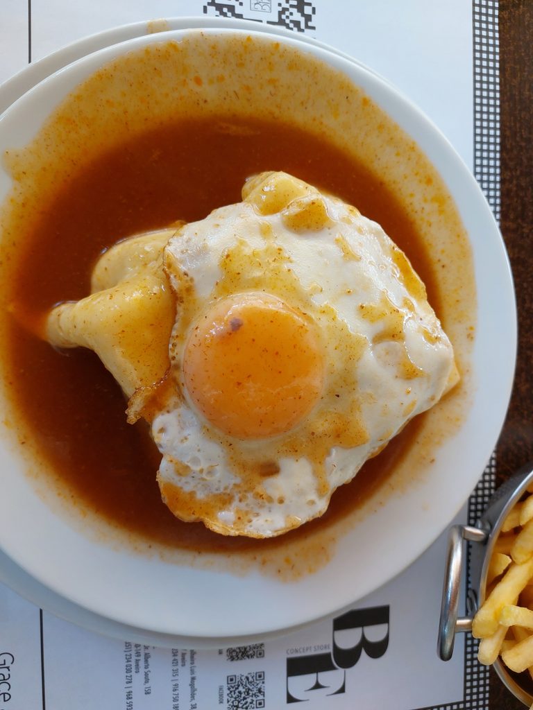 Francesinha met ei in een bad van saus, je kunt de friet aan de zijkant nog net zien.