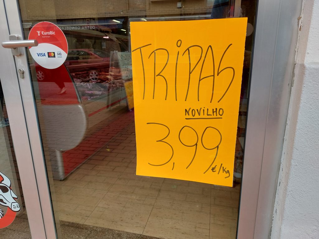 Deur van een slagerij in Espinho, Portugal, met een grote poster, tripas voor €3,99 per kilo